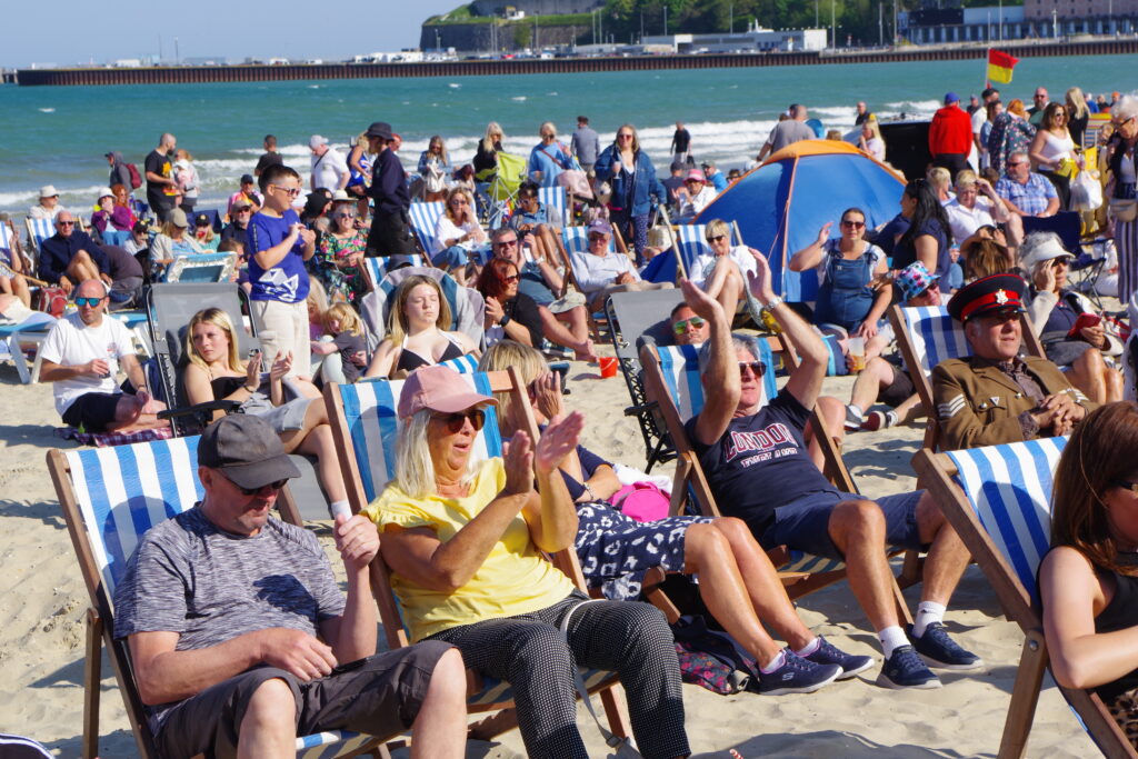 Crowd sat in deck chairs on the beach.